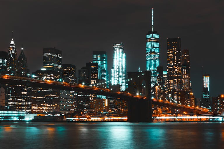 Captivating night skyline of New York City with Brooklyn Bridge and skyscraper reflections.